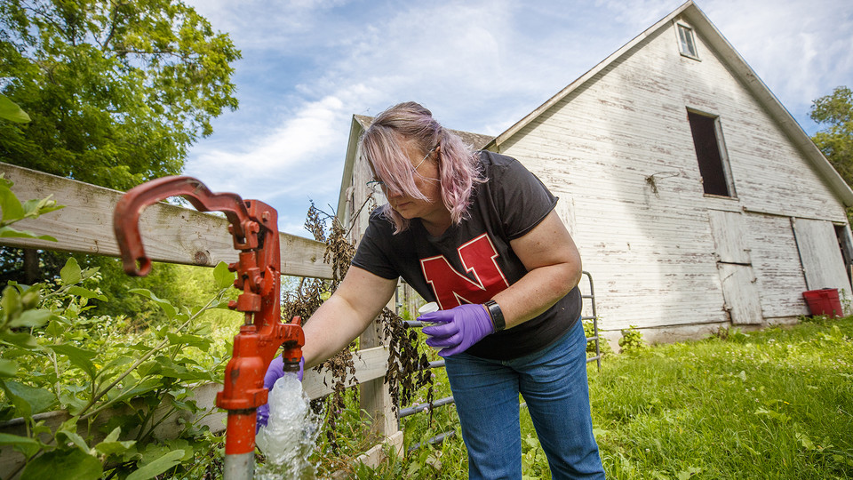 Jodi Sangster, a post-doc civil engineer specializing in environmental engineering, takes a water sample from a well spigot.