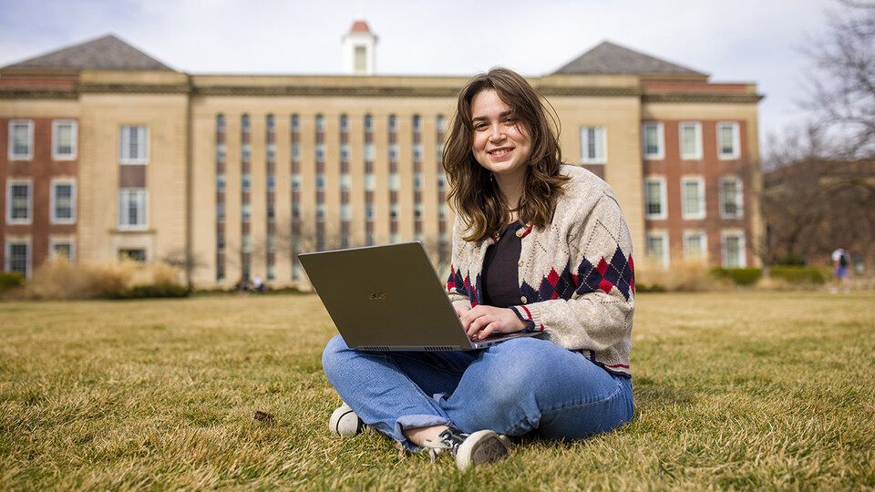 Ellie Woody sits on the green space in front of Love Library