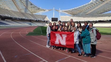 Twelve students, led by faculty members Georgia Jones and Dennis Perkey, pose with a Husker flag in the 2004 Olympic stadium