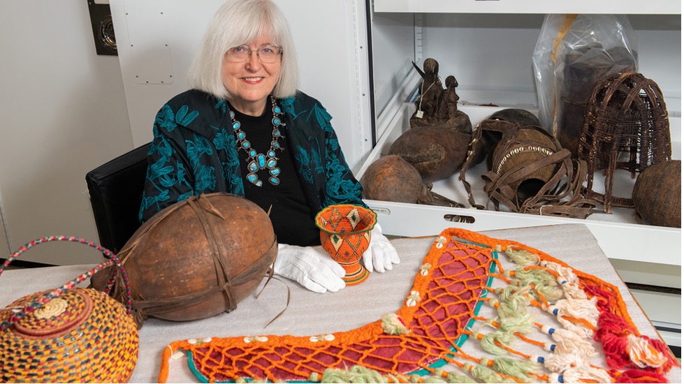 Priscilla Grew, director emerita, admires objects in the University of Nebraska State Museum’s African collection, including a horse breast collar purchased in Egypt. She holds a basket from Ethiopia collected about 1960. Also in the photo are a large basket from Sudan and a gourd from Tanzania.
