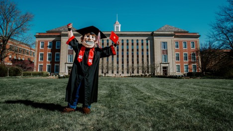 Husker Herbie wears a gown and holds a diploma. 
