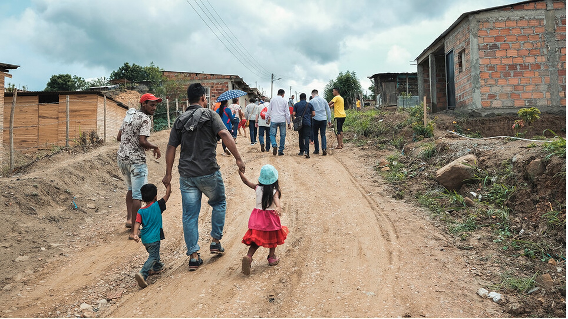 People walk with children in a third-world country village.
