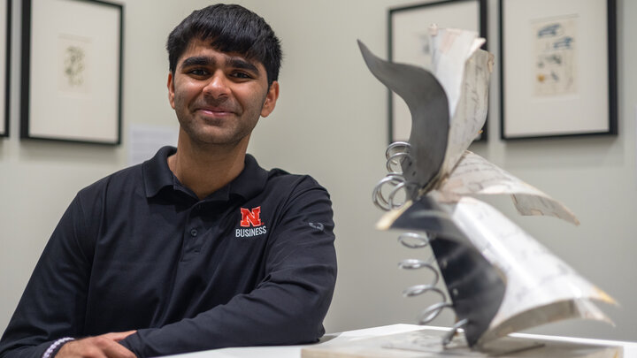 Student in black shirt near abstract metal miniature sculpture; framed art in background.