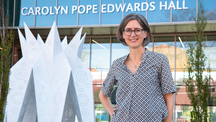 Person standing outside Carolyn Pope Edwards Hall near abstract metal sculpture.