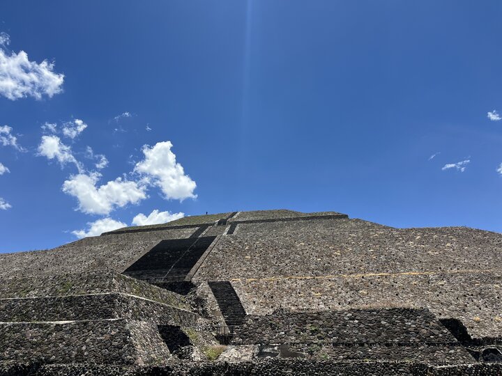 Stone pyramid under a bright blue sky with scattered white clouds.