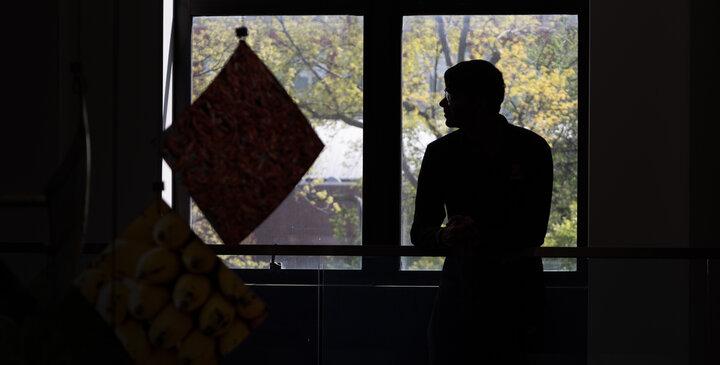 Silhouetted figure near a window, with trees visible outside. Hanging art from a mobile installation in front of student.
