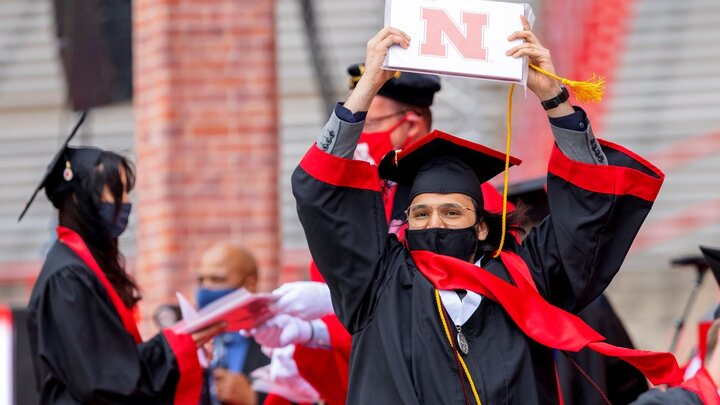 student in gown and cap graduating with N sign held above head