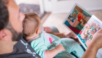 A father is reading a children’s book illustration to his baby.
